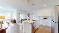 Located at 5155 Raglan St. in Hilliard, Ohio, this thoughtfully designed 2-bedroom, 2-bathroom residence offers a comfortable and modern single-floor layout. The open-concept kitchen and living area serves as the heart of the home, featuring sleek white cabinetry, a white subway tile backsplash, stainless steel appliances including a range, microwave, and refrigerator, and light quartz countertops. A central island with seating for two is illuminated by stylish gold pendant lights, creating an ideal space for both casual dining and entertaining. Wood-look flooring flows throughout the main living areas, adding warmth and continuity. The living room is bright and airy, with a large window offering outdoor views of the surrounding greenery. Both bedrooms are carpeted and restful, with the primary bedroom offering generous proportions and a dedicated walk-in closet outfitted with wire shelving for ample storage. Each of the two full bathrooms includes a tub-shower combination with a curved curtain rod, wood-look flooring, and clean white finishes. The second bathroom also features a white vanity with a light countertop. The overall aesthetic throughout is clean, contemporary, and inviting, with a neutral palette that creates a bright, welcoming atmosphere.