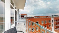 Situated in the heart of Columbus, Ohio's dynamic Short North Arts District, this single-floor space at 985 N High St offers a compelling blend of urban living and elevated outdoor access. The standout feature is a generously sized balcony enclosed by modern metal railings, providing sweeping panoramic views of the Columbus skyline and the eclectic surrounding neighborhood. From this elevated vantage point, residents can take in a broad cityscape stretching across tree-lined streets, mixed-use buildings, and the ever-evolving downtown skyline, including visible construction cranes that speak to the area's continued growth. String lights are strung across the rooftop terrace area visible from the balcony, adding a welcoming ambiance for evening gatherings. The building's distinctive orange brick exterior is prominently visible and contributes to the architectural character of the structure. Interior spaces, while more dimly captured, suggest a layout with defined rooms and subtle accent lighting details. The space is ideally positioned to take full advantage of its urban setting, offering residents immediate access to the restaurants, galleries, and entertainment venues that define the Short North corridor.