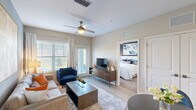 Located at 7580 Heron Circle in Vero Beach, Florida, this well-appointed one-bedroom, one-bathroom residence offers a smartly efficient layout across a single floor. The open-concept kitchen and living area forms the heart of the home, where wood-look flooring, soft neutral tones, and abundant natural light from large windows create a welcoming atmosphere. The kitchen is outfitted with white cabinetry, granite countertops, a peninsula island with bar seating, stainless steel appliances, and stylish pendant lighting overhead. The living area provides a comfortable gathering space anchored by a ceiling fan and a door leading to a private patio. The bedroom is a serene retreat featuring plush carpeting, a bold accent wall, large windows with outdoor views, a ceiling fan, and access to two closets. The bathroom includes a full tub-shower combination with white tile surround. Additional conveniences include an in-unit laundry area. Throughout the residence, clean architectural lines, recessed lighting, and a cohesive color palette contribute to a modern yet comfortable ambiance, making this Vero Beach home a refined and functional living space.