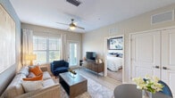 Located at 7580 Heron Circle in Vero Beach, Florida, this well-appointed one-bedroom, one-bathroom residence offers a smartly efficient layout across a single floor. The open-concept kitchen and living area forms the heart of the home, where wood-look flooring, soft neutral tones, and abundant natural light from large windows create a welcoming atmosphere. The kitchen is outfitted with white cabinetry, granite countertops, a peninsula island with bar seating, stainless steel appliances, and stylish pendant lighting overhead. The living area provides a comfortable gathering space anchored by a ceiling fan and a door leading to a private patio. The bedroom is a serene retreat featuring plush carpeting, a bold accent wall, large windows with outdoor views, a ceiling fan, and access to two closets. The bathroom includes a full tub-shower combination with white tile surround. Additional conveniences include an in-unit laundry area. Throughout the residence, clean architectural lines, recessed lighting, and a cohesive color palette contribute to a modern yet comfortable ambiance, making this Vero Beach home a refined and functional living space.