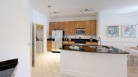 This single-floor residence offers a thoughtfully designed layout with a cohesive, contemporary aesthetic throughout. The kitchen serves as a functional centerpiece, featuring rich dark granite countertops, warm honey-toned wood cabinetry extending to the ceiling, and a full suite of stainless steel appliances, including a French door refrigerator, gas range, and built-in microwave. A peninsula with an undermount sink provides additional prep space and casual seating potential. Track lighting illuminates the room, while light ceramic tile flooring extends underfoot. A dedicated laundry area is conveniently accessible directly from the kitchen.

The living area is bright and inviting, with crisp white walls and room for comfortable seating arrangements. The bedrooms are carpeted and generously proportioned, each featuring clean white walls, good ceiling height, and direct access to well-appointed bathrooms. The bathrooms are finished with light tile flooring, warm wood vanities, white countertops, and chrome fixtures, maintaining a clean, neutral aesthetic throughout. The overall ambiance of the space is light, airy, and move-in ready, with a consistent design language that ties each room together seamlessly.