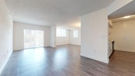 This single-floor residence offers a clean, functional layout with a bright and open atmosphere throughout. The expansive living area is a standout feature, finished with smooth hardwood-style flooring that reflects natural light streaming in through multiple large windows fitted with vertical blinds. A sliding glass door provides direct access to the outdoors, further enhancing the sense of openness. The textured ceiling adds a classic touch to the living space.

Adjacent to the living area, a dedicated dining space is defined by a pendant light fixture and a charming pass-through window that connects to the kitchen. The kitchen is thoughtfully designed with white cabinetry, sleek bar-pull hardware, speckled stone countertops, and matching hardwood-style flooring. A dishwasher is integrated into the cabinetry for added convenience.

The bedrooms are carpeted for comfort, offering a soft contrast to the hard-surface areas of the home. One bedroom features a closet with bi-fold doors and an additional adjoining door, providing flexible storage and access options. Each bedroom is well-lit by natural light through vertical-blind-covered windows.

The bathroom is finished in a clean, all-white palette, complete with a full soaking tub and tiled surround, offering a simple and functional space.