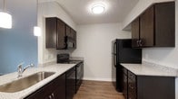Located at 3970 Brelsford Lane in Dublin, Ohio, this single-floor residence offers a functional and well-designed living space. The kitchen is a standout feature, showcasing rich dark espresso cabinetry that provides ample storage through both upper and lower cabinets. Granite-style countertops in a light speckled finish offer generous prep space and contrast beautifully with the dark cabinetry. The kitchen is equipped with a full suite of black appliances, including a range with an overhead microwave, a dishwasher, and a full-size refrigerator. A stainless steel sink adds a modern touch, while warm wood-look flooring grounds the space with a sense of warmth and durability. The layout is efficient and thoughtfully arranged, allowing for easy movement throughout the kitchen. Neutral gray walls and a textured ceiling keep the overall aesthetic clean and versatile, complementing the bold cabinetry tones. The space is well-lit with a flush-mount ceiling fixture, and natural light filters in through a nearby window. The overall ambiance is contemporary and practical, reflecting a home designed for comfort and everyday functionality in a well-established Dublin neighborhood.