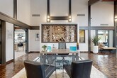 Located at 104 Yester Oaks Way in Greensboro, NC, this generously scaled single-floor property offers a thoughtfully designed interior with striking architectural character throughout. The space is defined by soaring double-height ceilings, bold dark structural beams, and an eclectic mix of materials that create a dynamic, contemporary atmosphere.

The main reception and lobby area serves as an impressive focal point, featuring rich mosaic tile flooring, dramatic floor-to-ceiling glazing, and a decorative laser-cut metal art installation that anchors the space. Wall sconces and abundant natural light filtering through expansive glass panels enhance the open, airy feel.

The living room showcases warm wood-planked ceilings, soft blue-toned walls, and light hardwood flooring, creating an inviting, relaxed atmosphere. A brick fireplace and large glass doors opening to outdoor views add depth and character. A game area with a billiards table offers additional recreational space beneath bold pendant lighting.

The kitchen features dark cabinetry paired with granite countertops and stainless steel appliances, lending a sleek, modern contrast. A separate kitchen-living area includes a decorative island with patterned tile accents, Edison bulb pendants suspended from a wood-beamed ceiling, and a white quartz countertop—blending function with distinctive style.