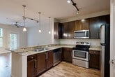 Located at 2200 Parklake Dr NE in Atlanta, Georgia, this one-bedroom, one-bathroom residence offers a well-designed single-floor layout with a thoughtful mix of finishes and functional spaces. The open-concept kitchen is a standout feature, showcasing rich dark cabinetry, granite countertops, a peninsula with pendant lighting, stainless steel appliances including a range, microwave, dishwasher, and refrigerator, and track lighting overhead. The kitchen flows seamlessly into the combined dining and living area, which is finished with wood-style flooring and features a ceiling fan, along with access to a private balcony through a glass door that brings in natural light and outdoor views. The bedroom is carpeted for comfort, featuring a window with wooded views and ample natural light. It is supported by multiple closets, including a spacious walk-in with built-in wire shelving. The bathroom is finished with tile flooring, a granite-topped dark vanity, a framed mirror, and a tiled tub-surround. Additional conveniences include a dedicated laundry area, a pantry, and a utility room, rounding out this efficiently organized and well-appointed Atlanta residence.