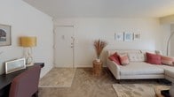 This single-floor residence presents a thoughtfully organized layout with distinct living zones. The kitchen is efficiently designed with light maple cabinetry extending to the ceiling, a stainless steel double-basin sink, laminate countertops, and white appliances including a gas range and dishwasher. Tile flooring completes the practical workspace.

The living area features neutral carpet and connects seamlessly to a dedicated dining space, which is equipped with a ceiling fan and overhead lighting. The dining area comfortably accommodates a round table with seating for four, with an adjacent mirror enhancing the sense of space.

Two bedrooms are carpeted and maintain a clean, neutral palette. Each room benefits from windows that allow natural light and provide outdoor views of surrounding greenery. The rooms offer sufficient space for standard furnishings and wall décor.

The full bathroom includes a shower-tub combination, a vanity with under-cabinet storage, a medicine cabinet with mirror, and tile flooring. White fixtures and neutral wall tones contribute to a clean, functional finish throughout.

Overall, the space offers a cohesive, understated aesthetic with practical finishes and a logical flow between rooms, making it a functional and comfortable single-level residence.