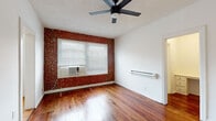 Located at 756 Normandie Ave in the heart of Los Angeles, this single-floor unit blends classic character with functional design. The living area immediately draws attention with its striking exposed brick accent wall, rich hardwood flooring, and a ceiling fan that anchors the room. Natural light filters in through blinds-covered windows, creating a warm and inviting atmosphere. A baseboard heater and window-mounted air conditioning unit ensure year-round comfort. The space flows seamlessly between rooms, with the open sightlines from the main living area providing a view into the kitchen beyond. The kitchen is outfitted with white cabinetry, a tile countertop, a stainless steel gas range, and a double-basin sink, all set atop warm terracotta tile flooring. A window above the counter allows natural light to brighten the workspace. The bathroom features a clean, classic aesthetic with white hex tile flooring, a pedestal sink, a medicine cabinet mirror, and a full bathtub with shower. Throughout the unit, the consistent use of hardwood floors, white walls, and ceiling fans creates a cohesive and practical living environment that reflects the character of this established Los Angeles neighborhood.