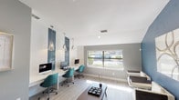 Located at 14901 E Mississippi Ave in Aurora, Colorado, this single-story community amenity space combines a functional business center with a comfortable lounge area, designed with a clean, modern aesthetic throughout. The space features light wood-look flooring that flows seamlessly between zones, contributing to a bright and cohesive atmosphere.

The business center section is well-equipped with a long, built-in white desk accommodating multiple workstations, each paired with teal ergonomic chairs. Striking vertical panels of deep blue subway tile serve as bold design accents behind each station, framed by industrial-style pendant lights that hang from the ceiling. Large windows along the exterior wall flood the workspace with natural light while offering views of the landscaped grounds.

The lounge area transitions naturally from the workspace, anchored by a bold slate-blue accent wall adorned with abstract artwork. Cream-colored swivel chairs and a dark coffee table create an inviting seating arrangement. Double glass doors open to an outdoor area, enhancing the sense of openness. Additional seating includes a plush blue accent chair, adding a pop of color against the neutral gray walls. Together, both areas deliver a polished, functional environment well-suited for work and relaxation.