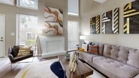 This two-story residence makes a strong architectural impression with its dramatic vaulted ceilings, most notably in the living room and primary bedroom. The living room is a standout space, featuring soaring double-height ceilings, tall windows that draw in generous natural light, and a white brick fireplace as a central focal point. Hardwood-style flooring runs through the main living areas, complementing the warm, neutral color palette throughout.

The dining area is positioned adjacent to the living room and features a full mirrored wall that visually expands the space, paired with pendant lighting overhead and wood flooring underfoot. The kitchen is outfitted with white cabinetry, grey laminate countertops, and white appliances including a refrigerator, electric range, and built-in microwave, all set on wood-look flooring.

The primary bedroom benefits from vaulted, angled ceilings and plush carpeting, creating a serene retreat. The bathroom features white tile, a soaking tub, a window for natural light, and an extended vanity with grey countertops. A dedicated laundry area with a full-size washer and dryer adds everyday convenience. A half bathroom is also present, tucked neatly within the layout.