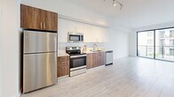 Located at 1080 NE 215th St in Miami, FL, this well-appointed one-bedroom, one-bathroom unit offers a clean, modern aesthetic with a bright and open layout. Light-toned wood-style flooring runs throughout the living spaces, complementing the crisp white walls and contributing to an airy, contemporary ambiance.

The open-concept kitchen and living area serves as the heart of the unit. The kitchen features a sleek two-tone design with white upper cabinetry and warm wood-finish lower cabinets, paired with stainless steel appliances including a refrigerator, range, microwave, and dishwasher. Light countertops and track lighting complete the polished look. The living area flows seamlessly from the kitchen and opens directly onto a private balcony through large sliding glass doors, allowing an abundance of natural light and outdoor views.

The bedroom is a well-proportioned, serene retreat with a large window framing views of the surrounding neighborhood and greenery. Three closets—including a generously sized walk-in with wire shelving—provide ample storage throughout the unit.

The bathroom is finished with large-format beige floor tiles, a wood-toned vanity with white countertop, and a standout tub-shower combination clad in bold, deep-blue glossy subway tile. An in-unit laundry area and an entrance hallway round out this thoughtfully designed Miami residence.