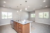 This single-floor residence is designed with an open, functional layout that seamlessly connects the kitchen, dining, and living areas. The kitchen serves as the centerpiece, showcasing rich cherry wood cabinetry, granite countertops, and a large island with a built-in sink and pendant lighting overhead. Stainless steel appliances, including a refrigerator, electric range, and built-in microwave, complement the space. A window above the cooking area frames pleasant outdoor views of greenery, adding natural light to the workspace. Hard surface flooring transitions into plush carpeting as the space opens into the living area, which benefits from multiple windows and a door providing additional outdoor access and natural light.

The bedroom is a well-proportioned, carpeted room with direct sightlines to the kitchen, and includes a generously sized walk-in closet outfitted with wire shelving and hanging rods along multiple walls. The bathroom features a dual-sink granite vanity with warm wood cabinetry, a full tub-shower combination, and easy-care hard surface flooring. Neutral gray walls throughout the unit create a cohesive, modern aesthetic.