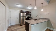 Located at 12 Wilkinson Way in Bluffton, South Carolina, this single-floor residence offers a well-designed open-concept layout with consistent wood-style flooring flowing throughout every room. The kitchen serves as a central highlight, showcasing dark espresso cabinetry, granite countertops, a peninsula with an undermount sink, and a full suite of stainless steel appliances including a refrigerator, range, and microwave. Pendant lighting above the peninsula adds a polished finishing touch, while flush-mount ceiling fixtures provide additional illumination. The open living area extends generously from the kitchen, offering ample room for various furniture arrangements. Bedrooms are bright and well-proportioned, each featuring ceiling fans, natural light from multiple windows, and wood-style flooring. A distinctive bay window configuration in one room enhances the sense of openness and brings in abundant natural light. A spacious walk-in closet with wire shelving provides generous storage. The bathrooms are finished with dark vanity cabinetry, granite countertops, and tiled tub-shower combinations with curved curtain rods. Clean neutral wall tones and white trim work unify the space, creating a cohesive and move-in ready environment throughout.