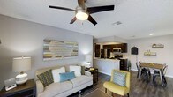 This single-floor space offers an open-concept layout that seamlessly connects the living area to the kitchen, creating a cohesive and functional environment. The living area features wood-style flooring, neutral gray walls, and a textured ceiling equipped with a ceiling fan, providing both style and comfort. Large baseboards and recessed ventilation contribute to the clean, finished look throughout.

The kitchen is positioned adjacent to the living area and is defined by dark espresso cabinetry that contrasts sharply with light countertops. Stainless steel appliances, including a refrigerator, microwave, and range, lend a modern, polished feel. A peninsula counter serves as a natural divider between the two spaces while offering additional prep or seating space.

The living area is well-proportioned, providing ample room for comfortable furnishings. A large decorative wall piece adds a focal point, while the neutral color palette is accented with teal and yellow tones throughout. Together, the two areas form a bright, contemporary space that balances everyday practicality with inviting design.