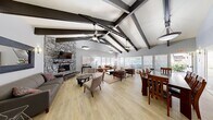 Located at 150 Cleaveland Rd in Pleasant Hill, CA, this community clubhouse is a thoughtfully designed gathering space that blends architectural character with practical amenities. The interior is anchored by soaring vaulted ceilings with striking exposed dark wood beams that run the length of the main floor, creating an open, airy atmosphere bathed in natural light from large windows along the exterior walls. Ceiling fans provide comfort throughout the generously proportioned space.

The living area is a standout feature, centered around a dramatic floor-to-ceiling stacked stone fireplace with a mounted television, offering a warm and inviting focal point. Multiple seating arrangements—including leather sofas and accent chairs—make the space well-suited for both relaxed gatherings and larger events. Light hardwood flooring flows seamlessly throughout.

Adjacent to the living area, a dedicated dining space accommodates a full wood dining table and chairs. The kitchen is efficiently appointed with warm wood cabinetry, dark granite countertops, a mosaic tile backsplash, and stainless steel appliances including a range, microwave, and refrigerator.

Outside, a sparkling swimming pool and adjacent spa are surrounded by a spacious patio, lush landscaping, and views of the surrounding residential community—ideal for outdoor recreation and socializing.