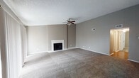 This single-floor residence offers a thoughtfully arranged layout with a generous living area at its center. The living room is a standout space, featuring plush wall-to-wall carpeting, neutral gray-toned walls, a textured ceiling, and a ceiling fan overhead. A white-framed fireplace serves as the room's focal point, while vertical blinds cover a sliding glass door that invites natural light into the space. The kitchen is well-equipped with rich dark wood cabinetry, granite countertops, wood-look flooring, and black appliances including a range, refrigerator, and dishwasher. A louvered pantry door adds classic character to the galley-style layout. The bedrooms are carpeted and finished with the same neutral gray palette, each featuring ceiling fans with light fixtures and windows with vertical blinds that allow for natural light. The bathroom presents a long vanity with granite countertops, dark wood cabinetry, a large framed mirror, and wood-look flooring, leading to a separate shower enclosure with glass doors. Throughout the residence, consistent finishes including textured ceilings, white baseboards, and neutral tones create a cohesive and functional living environment.