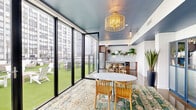 This thoughtfully designed rooftop amenity level seamlessly blends indoor comfort with outdoor recreation. The interior opens with an inviting corridor accented by a statement woven pendant light, polished concrete floors, and a large round mirror, setting a warm yet modern tone throughout. A cozy lounge area features polished concrete floors, a neutral sofa, natural wood accent stools, lush potted plants, and navy blue glass-fronted cabinetry, creating a relaxed, curated atmosphere. The kitchenette is well-appointed with warm wood cabinetry, penny-tile backsplash, a stainless steel refrigerator, built-in microwave, and a generous stone-topped island with woven bar stools — ideal for casual gatherings. A dining nook with a round white table and wood chairs sits beneath a rattan pendant light, overlooking the outdoor terrace through expansive floor-to-ceiling black-framed glass doors that fold fully open. The outdoor terrace is covered in lush artificial turf and furnished with clusters of white Adirondack chairs, low tables, and lawn games, all framed by open urban skyline views. Accessible restrooms with clean white subway tile and soft blue accents complete the space. Throughout, a cohesive blue-painted ceiling ties every area together with a bold, design-forward touch.