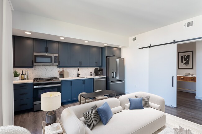 Studio Living Area and Kitchen featuring blue cabinets and marble-style backsplash and countertops. - Fallyn