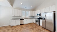 Located in North Myrtle Beach, South Carolina, this single-story home offers a clean, modern design with an open and airy layout throughout. The living area welcomes you with soaring vaulted ceilings, a ceiling fan, and a paneled front door with a transom window above, allowing natural light to pour in and create a bright, inviting atmosphere. Warm hardwood-style flooring flows seamlessly through the main living spaces and bedrooms, tying the home together with a cohesive look.

The kitchen is well-appointed with crisp white shaker-style cabinetry, granite-look countertops, and a full suite of stainless steel appliances including a range, over-the-range microwave, dishwasher, and French door refrigerator. Recessed lighting and vaulted ceilings enhance the sense of space, while a window above the sink brings in additional natural light.

The bedrooms are generously sized, each featuring large windows with blinds and ceiling fans, offering a calm and comfortable retreat. The bathrooms are finished with granite-topped white vanities and hardwood-style flooring. One bathroom includes a tub-shower combination, while another features a walk-in shower with glass enclosure. Throughout, the home maintains a neutral color palette, lending a fresh, move-in-ready appeal ideal for the North Myrtle Beach lifestyle.