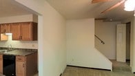 This two-story residence offers a practical and functional layout spread across two levels. The main floor features a central open area with light-toned walls and tile flooring, creating a clean and neutral living environment. A staircase with a decorative wrought iron railing provides access to the upper floor, serving as a subtle architectural accent within the space. Adjacent to the main area, the kitchen is equipped with warm wood cabinetry and dark countertops, providing ample storage and workspace for everyday use. The kitchen is separated from the main living area by a partial wall opening, allowing for a sense of connection between the two spaces while maintaining defined zones. The ceiling features a textured finish, and a ceiling fan is partially visible, contributing to the home's practical amenities. Neutral wall tones and tile flooring throughout the main level lend the space a clean, move-in-ready appearance. The layout is straightforward and efficient, with clearly defined areas that make good use of the available footprint. The second floor, accessible via the interior staircase, expands the living capacity of the home and provides additional private space above the main level.