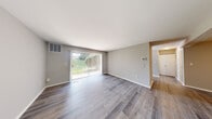 This single-floor residence offers a clean, modern aesthetic throughout its thoughtfully designed layout. The spacious living area is finished with durable wood-style plank flooring and painted in a neutral gray palette, creating a bright and versatile space. A full-height sliding glass door with vertical blinds fills the room with natural light while providing direct views of the surrounding greenery outside. An adjacent dining or secondary living area features warm-toned walls and a ceiling fan, lending a comfortable, functional atmosphere.

The kitchen is well-equipped with dark shaker-style cabinetry, light countertops, a subway tile backsplash, and a full suite of stainless steel appliances including a refrigerator, gas range, built-in microwave, and dishwasher. A window above the sink brings in additional natural light.

The bedrooms are finished with plush carpet and feature ample wall space, with one room including a mirrored door and access to a closet. Natural light enters through standard windows with blinds. The bathroom is tastefully updated with a tiled tub surround in a stacked mosaic pattern, modern vanity, and tile flooring, combining style with practicality throughout.