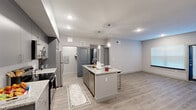 Located at 10742 Freehill Street in Houston, TX, this single-story home presents a contemporary design with a neutral color palette and wood-look flooring throughout the main living areas. The open-concept layout connects the kitchen and living space seamlessly, creating a functional and inviting environment.

The kitchen serves as a central gathering point, anchored by a large island with granite countertops, an undermount sink, and pendant lighting overhead. Gray cabinetry extends to the ceiling, providing ample storage, while stainless steel appliances—including a range, microwave, and refrigerator—complete the modern aesthetic. The adjacent living and dining area benefits from natural light through window treatments and provides direct access to the front entry.

The bedrooms feature plush carpeting, ceiling fans, and windows with blinds that allow for adjustable natural light. The primary suite includes a well-appointed en-suite bathroom with a granite-topped vanity, a glass-enclosed shower, built-in shelving, and direct access to a spacious walk-in closet outfitted with multi-tier wire shelving systems. A secondary bathroom offers a soaking tub and shower combination with large-format tile surround and a granite vanity. Throughout, the home maintains a clean, modern character with consistent finishes.