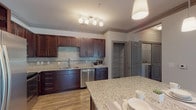 Located at 3055 Carrington Mill Blvd in Morrisville, NC, this single-floor residence offers a thoughtfully designed open-concept layout with a clean, modern aesthetic throughout. The living area is expansive and welcoming, featuring wood-look luxury vinyl plank flooring, crown molding, and ceiling fans that add both style and function. Multiple windows bathe the space in natural light and offer pleasant outdoor views.

The kitchen is a standout feature, outfitted with rich dark wood cabinetry, granite countertops, a tile backsplash, and a full suite of stainless steel appliances including a refrigerator, range, microwave, and dishwasher. A central island provides additional prep and dining space, while pendant lighting adds a refined touch. A built-in pantry offers generous storage.

The bedrooms are generously sized with plush carpet flooring, ceiling fans, and multiple windows that enhance the airy feel. Ample closet space, including a walk-in, ensures practical storage solutions.

The bathrooms are well-appointed with dark wood vanities, light stone countertops, and wood-look flooring. One bathroom features a soaking tub with shower, while another includes a glass-enclosed shower, both finished with clean, neutral tones that contribute to the overall polished ambiance of the residence.