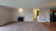 Located at 2405 S Star Lake Road in Federal Way, Washington, this single-floor unit offers a practical and comfortable layout with a variety of functional features throughout. The living area is anchored by a tile-surround fireplace with a classic white mantle, providing a focal point to the room. Plush carpeting extends through the living and bedroom spaces, while hardwood-style flooring adds warmth to the entryway and kitchen areas. A decorative ceiling light fixture enhances the dining or entry area, which opens toward a sliding glass door leading to an outdoor balcony with views of the surrounding neighborhood. The kitchen is well-equipped with rich dark wood cabinetry, a peninsula with countertop seating, a window overlooking greenery, and black appliances including a refrigerator and dishwasher. A dedicated laundry area is conveniently accessible from the main living space. The bedrooms are carpeted and receive natural light through window blinds, with views of lush outdoor trees and neighboring rooftops. The bathroom features tile flooring, a tub-shower combination, a vanity with rich wood cabinetry, and a lighted mirror. Textured ceilings are consistent throughout, and the neutral color palette creates a clean, move-in ready environment.