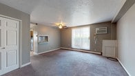 This single-floor unit at 5327 Northfield Rd in Bedford Heights, Ohio offers a well-organized layout with a variety of functional living spaces. The living room is generously sized, featuring plush carpeting, neutral gray walls, a textured ceiling, and a ceiling fan. A large sliding glass door fills the room with natural light and provides outdoor access, while a wall-mounted air conditioning unit and baseboard heating ensure year-round comfort. A convenient pass-through window connects the living area to the kitchen, enhancing the open feel of the space. The galley-style kitchen is efficiently designed with dark cabinetry, granite-look countertops, tile flooring, and a tiled backsplash, along with a window that brings in additional natural light. The unit includes two carpeted bedrooms, each with baseboard heating and windows fitted with vertical blinds. One bedroom features a closet with built-in shelving. Two bathrooms serve the unit: a full bathroom with a tub-shower combination, tile surround, vanity with cabinetry, and a mirrored medicine cabinet, and a half bathroom with a pedestal sink and a grab bar. Clean white trim and a consistent neutral color palette unify the overall aesthetic of the space.