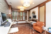 Located at 1925 Monroe Dr NE in Atlanta's vibrant Midtown area, this business center offers a thoughtfully designed single-floor space that balances functionality with sophisticated style. Rich hardwood flooring flows throughout, complemented by warm dark wood trim and framing that lend a cohesive, upscale character to the entire space.

The main work area is equipped with multiple computer workstations arranged along wall-mounted desks, accompanied by modern adjustable bar-height seating. Decorative drum pendant lighting and recessed ceiling lights provide ample illumination, while textured accent walls add visual depth and interest. Plantation shutters on large windows allow natural light to filter in while maintaining privacy, with views of surrounding greenery visible through the slats.

A comfortable seating nook features rich cognac leather chairs arranged around a small side table, creating an inviting area for reading or informal meetings. Built-in open shelving units display an assortment of magazines and publications, making them easily accessible to visitors. Artwork and a distinctive geometric mirror accent the walls, contributing to the refined ambiance.

Restroom facilities are conveniently accessible directly from the space through dark wood-framed frosted-glass doors. The overall atmosphere is professional yet welcoming, making this business center a well-appointed resource for productivity and convenience.