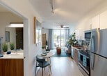 Located at 5375 NW 7th Street in Miami, FL, this single-floor studio offers a thoughtfully designed open-concept layout that seamlessly integrates the living, sleeping, and dining areas into one cohesive space. Light wood-style tile flooring runs throughout, complementing the bright, white walls and lending the unit a clean, contemporary feel.

The kitchen is outfitted with stainless steel appliances — including a refrigerator, electric range, microwave, and dishwasher — paired with sleek white upper cabinetry, warm wood-toned lower cabinets, and a light countertop surface. A compact dining area with a round table sits conveniently adjacent to the kitchen.

The living and sleeping area benefits from generous natural light, courtesy of floor-to-ceiling sliding glass doors that open onto a private balcony overlooking the surrounding Miami landscape. A ceiling fan keeps the space comfortable, while a bamboo room divider provides a subtle separation between the sleeping and living zones. An open closet offers convenient storage within the main area.

The bathroom features a frameless glass-enclosed walk-in shower finished with large-format stone-look tile and a rainfall showerhead, conveying a spa-like atmosphere. The overall ambiance of the unit is light, airy, and modern — well-suited to the Miami lifestyle.