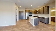This single-floor residence showcases a clean, contemporary design throughout, with a neutral warm-beige color palette and quality finishes that create a cohesive and inviting atmosphere. The open-concept kitchen serves as a central highlight, featuring rich dark-toned cabinetry extending to the upper walls, white quartz countertops, a central island, and a full suite of stainless steel appliances including a refrigerator, electric range, microwave, and dishwasher. Light-toned luxury vinyl plank flooring runs through the main living and kitchen areas, complementing the bright recessed lighting overhead. The living area offers generous proportions, with large windows fitted with blinds that invite abundant natural light and views of the surrounding neighborhood. Bedrooms are finished with plush neutral carpeting and ceiling fans, each featuring windows that further enhance the sense of light and openness. The primary bathroom is particularly well-appointed, presenting dark wood cabinetry, a white countertop vanity, a large mirror with overhead lighting, and tile flooring, with an adjacent walk-in closet. A secondary full bathroom mirrors this refined styling. The dedicated laundry room accommodates full-size side-by-side washer and dryer units with overhead wire shelving for added storage. An exterior door from the living area provides convenient outdoor access, completing this well-designed residence.
