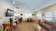 Located at 3100 Old Providence Ln in Columbus, Ohio, this single-floor community space offers a thoughtfully designed open-concept layout that seamlessly integrates a kitchen, dining room, and living room into one cohesive environment. The interior is finished with warm neutral tones, crown molding, and recessed lighting throughout, contributing to a bright and welcoming atmosphere. Ceiling fans provide comfortable air circulation across the space.

The kitchen is well-equipped with white cabinetry featuring wood-tone trim, dark granite-style countertops, a full suite of appliances including a refrigerator, electric range, microwave, and a double stainless steel sink. A breakfast bar with bar seating extends the kitchen's functionality and connects it to the dining and living areas.

The dining area accommodates a full-size table with multiple chairs and benefits from abundant natural light streaming through large windows fitted with white blinds. Colorful wall art adds a lively touch to the space.

The living area features plush carpeted flooring, comfortable seating including a sofa and accent chairs, and access to the outdoors via French doors that overlook a pool area. A water cooler station and a flat-screen TV round out the amenities, making this a versatile and inviting communal gathering space.