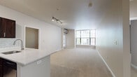 Located at 931 NW 11th Ave in Portland, Oregon, this single-floor unit sits in the heart of the vibrant Pearl District. The open-concept living and dining area is finished with neutral-toned carpet and bathed in natural light from large windows that frame views of the surrounding urban streetscape. Track lighting overhead adds a modern touch and ensures the space is well-lit throughout. A wall-mounted HVAC unit provides climate control directly in the living area.

The kitchen is a standout feature, outfitted with rich dark-brown shaker-style cabinetry, a classic white subway tile backsplash, light stone countertops, and a full suite of stainless steel appliances including a refrigerator, range, and built-in microwave. Light wood-look flooring grounds the kitchen and provides a clean contrast to the cabinetry. A breakfast bar peninsula connects the kitchen to the living area, enhancing the open flow of the floor plan.

The bedroom is generously proportioned with large windows, plush carpet, and a walk-in closet. The bathroom is cleanly appointed with wood-look flooring, a marble-style vanity countertop, dark cabinetry, and a full tub and shower combination with brushed nickel fixtures and grab bar. The layout is efficient and functional, making excellent use of the available space throughout.