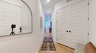 This thoughtfully designed 2-bedroom, 2-bathroom single-floor residence delivers a clean, modern aesthetic throughout. Light hardwood flooring flows continuously from the welcoming entry hallway — accented by an arched mirror and panel-style doors with matte black hardware — into the main living areas. The open-concept kitchen features slate-toned cabinetry, white quartz countertops, stainless steel appliances, a subway tile backsplash, and a central island with an undermount sink, offering both functionality and style. The adjacent dining nook is bathed in natural light from large windows dressed with neutral blinds and drapery. The living room continues the bright, airy feel with corner windows framing outdoor greenery, creating an inviting gathering space. The primary bedroom is a serene retreat with warm hardwood floors, soft neutral walls, and a ceiling fan. Its en-suite bathroom offers a glass-enclosed walk-in shower, dual-sink vanity with illuminated mirrors, and sleek dark cabinetry. The second bedroom features generous windows with outdoor views and direct closet access. Two dedicated closets provide ample storage throughout. Recessed lighting and a consistent modern design language tie the entire space together cohesively.
