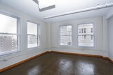 This single-floor unit blends industrial character with functional design, offering a layout that accommodates comfortable urban living. The open living area features polished concrete floors that reflect natural light streaming in through large windows, which frame notable views of surrounding city buildings. Exposed ductwork along the ceiling reinforces the loft-like, industrial aesthetic throughout the common areas. A pass-through counter connects the living space to the galley-style kitchen, which is equipped with light wood cabinetry, dark countertops, a double sink, and stainless steel appliances including a refrigerator, range, and dishwasher. Two windows in the kitchen allow additional natural light and continued city views.

The bedrooms feature warm, neutral carpet and ceiling fans with lighting. One bedroom benefits from a corner window configuration, while another includes a closet and direct access to the hallway. Two bathrooms serve the unit: one includes a walk-in glass shower, wood-toned vanity, and polished concrete flooring, while the second offers a full soaking tub with shower combination, a wide vanity with ample counter space, and a large mirror. Warm wood baseboards throughout provide a grounding contrast to the crisp white walls.