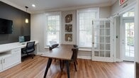 Located at 325 Marymeade Dr in Summerville, SC, this single-floor space combines functional design with refined aesthetics. Warm hardwood flooring runs throughout, tying each area together cohesively. Crown molding adds a classic architectural touch to the ceilings, enhancing the overall polish of the interior.

The co-working area serves as a central hub, featuring a built-in white desk station accommodating multiple workspaces, complete with cabinetry and a wall-mounted flat-screen display set against a bold dark accent wall. Pendant lighting casts a warm glow over the workstations, while a large window invites ample natural light. A rustic wood conference table with studded leather chairs occupies a dedicated meeting zone, accompanied by French glass doors that lend an open, airy quality to the space. Decorative wall art in natural, organic textures adds visual interest.

A welcoming entry area features curated décor, including a round mirror, accent lamp, and abstract wall art, creating a refined first impression. Adjacent to this is a dedicated package room housing smart parcel lockers, offering a practical and secure solution for deliveries. Together, these spaces reflect a well-appointed, community-oriented environment designed for both productivity and convenience.