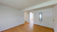 This single-floor unit is characterized by warm hardwood flooring that runs consistently throughout every room, creating a cohesive and clean aesthetic. The entry area opens into a spacious living space with white walls, a structural beam detail at the ceiling, and a wall sconce. A narrow window brings in a touch of natural light, while an open passage connects the living area to the rest of the unit.

The kitchen is laid out in a U-shaped configuration, offering ample cabinetry in a rich dark wood finish, light-toned countertops, and a full suite of white appliances including a refrigerator, dishwasher, and range. A window above the sink provides natural light to the workspace.

The bedrooms are generously sized, each equipped with ceiling fans and baseboard heating. Multiple louvered bi-fold closet doors offer substantial storage. Windows in each bedroom allow for natural light and outdoor views. A dedicated laundry closet houses a stacked washer and dryer unit, adding notable in-unit convenience.

The full bathroom includes a tub-shower combination, toilet, and a vanity with wood cabinetry, all finished with hardwood-style flooring. The overall ambiance is clean, functional, and well-maintained.