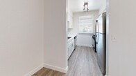 Located in Millcreek, Utah, this 2-bedroom, 2-bathroom single-floor residence offers a clean, modern aesthetic with thoughtful finishes throughout. The open living room serves as the heart of the home, featuring warm wood-look vinyl flooring, a ceiling fan with light fixture, and a standout tiled fireplace with a classic white mantel — an inviting focal point for the space. The living area flows naturally into the rest of the home, with ample natural light filtering in through windows dressed with horizontal blinds. The galley-style kitchen is efficiently designed with white shaker cabinetry, a stainless steel refrigerator and range, a window above the sink, and track lighting overhead. Both bedrooms are carpeted and comfortably sized, each equipped with ceiling fans. The primary bedroom offers generous proportions, while the second bedroom includes a built-in sliding-door closet. The bathrooms are well-appointed; one features a tub-shower combo with grey subway tile surround and wood-look tile flooring, while the other includes a white vanity with quartz-style countertop and brushed nickel hardware. A connecting hallway ties the layout together seamlessly, making this a practical and well-finished home.