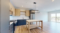 Located at 4 N Hickory Ave in Arlington Heights, IL, this thoughtfully designed 2-bedroom, 1-bathroom residence offers a modern aesthetic with high-quality finishes throughout. The open-concept kitchen and living area serves as the heart of the home, showcasing a striking two-tone kitchen with navy lower cabinets, natural wood upper cabinetry, and crisp white countertops. A full suite of stainless steel appliances — including a gas range, built-in microwave, dishwasher, and French door refrigerator — complement the space, while a bold industrial pendant light fixture anchors the kitchen island area. Light hardwood flooring flows seamlessly throughout the entire residence, enhancing the bright, airy atmosphere. The primary bedroom features sliding glass doors opening to a private balcony with expansive views of the surrounding Arlington Heights neighborhood. The second bedroom enjoys generous natural light through a large picture window with similar outdoor views. The full bathroom is finished with white subway tile surround, a soaking tub, and neutral tile flooring. Additional highlights include a spacious walk-in closet with built-in shelving and a dedicated utility room, rounding out this well-appointed and efficiently designed home.