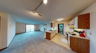 This single-floor residence offers a practical and functional layout designed for comfortable everyday living. The heart of the home is an open-concept living and kitchen area, where plush carpeting extends throughout the spacious living room, which is brightened by a sliding glass door that invites natural light. A peninsula-style kitchen anchors the space, featuring warm wood cabinetry paired with white upper cabinets, light countertops, a double sink, a dishwasher, a white electric range, and a refrigerator — all set atop easy-care vinyl flooring. Track lighting overhead adds a functional touch to this central area. The bedrooms are carpeted and well-proportioned, each featuring windows that bring in natural light. One bedroom includes access to a built-in shelved closet, providing organized storage. The full bathroom is neatly appointed with a tub-shower combination, a single vanity with a broad mirror, and tile flooring. A dedicated laundry room houses a full-size top-loading washer and dryer alongside a water heater. Completing the home is an attached single-car garage with an automatic opener, offering convenient and secure parking. Warm wood-tone trim and doors are consistent throughout, lending a cohesive character to the entire space.