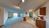 This single-floor residence offers a practical and functional layout designed for comfortable everyday living. The heart of the home is an open-concept living and kitchen area, where plush carpeting extends throughout the spacious living room, which is brightened by a sliding glass door that invites natural light. A peninsula-style kitchen anchors the space, featuring warm wood cabinetry paired with white upper cabinets, light countertops, a double sink, a dishwasher, a white electric range, and a refrigerator — all set atop easy-care vinyl flooring. Track lighting overhead adds a functional touch to this central area. The bedrooms are carpeted and well-proportioned, each featuring windows that bring in natural light. One bedroom includes access to a built-in shelved closet, providing organized storage. The full bathroom is neatly appointed with a tub-shower combination, a single vanity with a broad mirror, and tile flooring. A dedicated laundry room houses a full-size top-loading washer and dryer alongside a water heater. Completing the home is an attached single-car garage with an automatic opener, offering convenient and secure parking. Warm wood-tone trim and doors are consistent throughout, lending a cohesive character to the entire space.