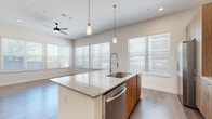 This well-appointed 2-bedroom, 2-bathroom residence offers a thoughtfully designed single-level layout that maximizes both function and style. The open-concept kitchen and living area serves as the heart of the home, anchored by a large central island with striking granite countertops and an undermount sink with a professional-style pull-down faucet. The kitchen is outfitted with warm wood-tone cabinetry, a subway tile backsplash, and a full suite of stainless steel appliances, including a refrigerator, range, microwave, and dishwasher. Pendant lighting above the island complements the recessed lighting and ceiling fan overhead. The living area is bright and open, benefiting from multiple large windows dressed with horizontal blinds that invite generous natural light. Hardwood-style flooring flows consistently throughout the residence, lending a clean, cohesive aesthetic. A well-proportioned hallway connects the bedrooms, each featuring ceiling fans, natural light, and dedicated closets. The primary bedroom is comfortably sized with its own access to storage. Both bathrooms echo the home's design language, featuring granite-topped wood vanities and tile-surround tub-shower combinations. The overall ambiance is contemporary, clean, and move-in ready.