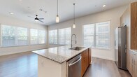 This well-appointed 2-bedroom, 2-bathroom residence offers a thoughtfully designed single-level layout that maximizes both function and style. The open-concept kitchen and living area serves as the heart of the home, anchored by a large central island with striking granite countertops and an undermount sink with a professional-style pull-down faucet. The kitchen is outfitted with warm wood-tone cabinetry, a subway tile backsplash, and a full suite of stainless steel appliances, including a refrigerator, range, microwave, and dishwasher. Pendant lighting above the island complements the recessed lighting and ceiling fan overhead. The living area is bright and open, benefiting from multiple large windows dressed with horizontal blinds that invite generous natural light. Hardwood-style flooring flows consistently throughout the residence, lending a clean, cohesive aesthetic. A well-proportioned hallway connects the bedrooms, each featuring ceiling fans, natural light, and dedicated closets. The primary bedroom is comfortably sized with its own access to storage. Both bathrooms echo the home's design language, featuring granite-topped wood vanities and tile-surround tub-shower combinations. The overall ambiance is contemporary, clean, and move-in ready.