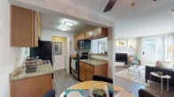 This single-floor residence offers a thoughtfully designed layout that integrates living, dining, and kitchen areas in a cohesive open-concept arrangement. The kitchen is well-equipped with warm honey-toned cabinetry, granite countertops, and a full suite of stainless steel appliances, including a refrigerator, electric range with microwave above, and dishwasher. Wood-look plank flooring runs throughout the main living areas, adding warmth and continuity.

The living room serves as a central gathering space, highlighted by a corner fireplace with a clean white surround and crown molding details. A sliding glass door fills the room with natural light and provides direct access to a private outdoor balcony with wooded views. Track lighting and a ceiling fan complement the space's functionality.

The bedroom features plush carpeting, generous natural light from large windows overlooking greenery, and a sliding-door closet offering ample storage. The bathroom is finished with granite countertops, warm wood cabinetry, a wide vanity mirror framed by bright lighting, and teal accent walls that add a distinctive character. Overall, the space presents a comfortable and cohesive living environment with quality finishes throughout.