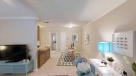 Located at 1906 Guess Rd in Durham, North Carolina, this single-floor residence offers a thoughtfully designed living space with a clean, cohesive aesthetic throughout. The interior is finished with warm neutral tones on the walls, complemented by white crown molding that adds a touch of classic elegance to each room.

The main living area is carpeted and generously proportioned, providing ample room for both relaxation and functional use. A built-in wooden counter or bar-height divider subtly separates the living space from an adjacent area, adding architectural interest while maintaining an open feel. The dining area, positioned centrally, is defined by a patterned area rug and is accented by a decorative mirror on the wall, creating a welcoming focal point.

The layout flows naturally toward interior doors that lead to additional rooms, including what appears to be a bathroom with visible mirrored cabinetry. Ceiling-mounted lighting fixtures illuminate the space evenly, while the overall layout promotes a sense of connectivity between rooms. White trim and baseboards throughout lend a crisp, finished look. The space strikes a balance between comfort and practicality, making it a functional and inviting single-story home in the Durham area.