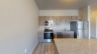 This single-floor unit at 2016 Main Ave S in Brookings, South Dakota presents a clean, contemporary design with a thoughtfully arranged open-concept layout. Light-toned luxury vinyl plank flooring runs throughout the main living areas, complementing the neutral gray wall palette and contributing to a bright, cohesive aesthetic.

The kitchen is a functional centerpiece, equipped with a full suite of stainless steel appliances including a refrigerator, electric range, over-the-range microwave, and dishwasher. Light wood cabinetry pairs with granite-style countertops, and a peninsula provides additional workspace and separates the kitchen from the open living area. Natural light enters through multiple windows fitted with blinds and vertical panel treatments.

The living space is generously proportioned, offering an open floor plan with access to additional rooms through paneled interior doors. A wall-mounted air conditioning unit provides supplemental climate control alongside baseboard heating visible in the bedroom, which features a window with outdoor views.

The bathroom is well-appointed with wood-toned cabinetry, a granite-top vanity, a framed mirror, and a full tub-shower combination with chrome fixtures, set against warm wood-look tile flooring and taupe walls.