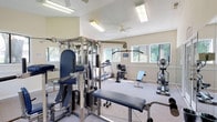 This fitness center offers a bright and welcoming environment designed to support a well-rounded workout routine. The space features vaulted ceilings that create an open, airy atmosphere, complemented by ceiling fans that promote comfortable airflow during exercise. Large windows line the walls, flooding the room with natural light and providing pleasant views of the surrounding greenery outdoors.

The facility is comprehensively equipped for both cardiovascular and strength training. Cardio equipment includes treadmills, a recumbent stationary bike, and an elliptical machine, providing ample options for aerobic exercise. For strength training, a multi-station cable machine and weight system serve as the centerpiece, accompanied by a weight bench and a selection of free weights, including dumbbells.

Full-length wall mirrors enhance the sense of space while allowing users to monitor their form during workouts. The neutral, warm-toned walls and light carpeted flooring contribute to a clean and comfortable aesthetic throughout. French doors provide access to the exterior, adding convenience and further connecting the interior to the outdoors. The layout is thoughtfully organized to maximize usable floor space while keeping equipment easily accessible.
