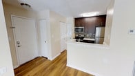 This single-floor residence offers a thoughtfully designed layout with a clean, modern aesthetic. The kitchen is a standout feature, showcasing rich dark-stained cabinetry paired with stainless steel appliances, including a refrigerator, range, and built-in microwave. A mosaic tile backsplash adds a stylish accent behind the range, while the peninsula-style countertop with a crisp white surface provides additional workspace and a natural separation between the kitchen and the adjacent living area. Warm hardwood-style flooring runs throughout, lending continuity and a welcoming ambiance to the space. The neutral, light-toned walls complement the darker cabinetry and create a bright, open feel. Flush-mount ceiling lighting ensures the kitchen remains well-lit. A pair of closet doors visible near the entryway suggest ample built-in storage options. The overall design balances functionality with contemporary style, making the space both practical and visually appealing. The seamless flow between areas enhances the sense of openness, making this a comfortable and well-organized single-floor living space.