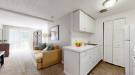 Located at 500 Main St in East Haven, Connecticut, this single-floor residence offers a practical and well-organized layout across two bedrooms, one bathroom, a living room, and a dedicated laundry area. The living room provides a comfortable, open feel with neutral-toned walls, plush carpeting, and a seamless connection to the kitchen, which features white cabinetry and appliances. The spacious primary bedroom is generously sized, offering room to move freely, and includes carpeted flooring, a window that invites natural light, and a wall-mounted air conditioning unit for year-round comfort. A sliding glass door in the bedroom area opens to an exterior view, adding brightness and a sense of openness. The second bedroom shares the same clean, neutral aesthetic. The full bathroom is bright and well-appointed, featuring a tub-shower combination with crisp white tile and wood-look flooring. White cabinetry with a utility sink anchors the kitchen area, with an adjacent closet and access to the carpeted laundry room, providing added convenience. Throughout the residence, a consistent palette of warm neutrals and white trim creates a cohesive, move-in-ready atmosphere suited for comfortable everyday living.