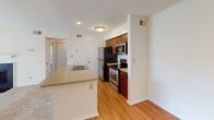 Located at 1004 Columbine Dr in Frederick, Maryland, this single-floor residence offers a thoughtfully designed layout with a clean, neutral aesthetic throughout. The kitchen serves as a central highlight, featuring rich cherry wood cabinetry, granite-look countertops, and a full suite of stainless steel appliances including a refrigerator, electric range, and over-the-range microwave. A peninsula with an integrated sink provides additional prep space and creates a natural division between the kitchen and the adjacent living area. The living space is finished with warm, light-toned carpeting and connects seamlessly to the kitchen via light hardwood-style flooring, giving the open-concept area a welcoming, cohesive feel. The bedroom is generously proportioned, with soft carpeting underfoot and multiple windows fitted with horizontal blinds that allow for ample natural light while maintaining privacy. The full bathroom is well-appointed with a cherry wood vanity, white countertop, a large mirror with overhead lighting, and a full-sized soaking tub with shower combination. Warm-toned flooring ties the bathroom together, complementing the rich cabinetry tones seen throughout the unit. The overall design is practical and consistent, making this a comfortable and functional single-level living space in Frederick, MD.